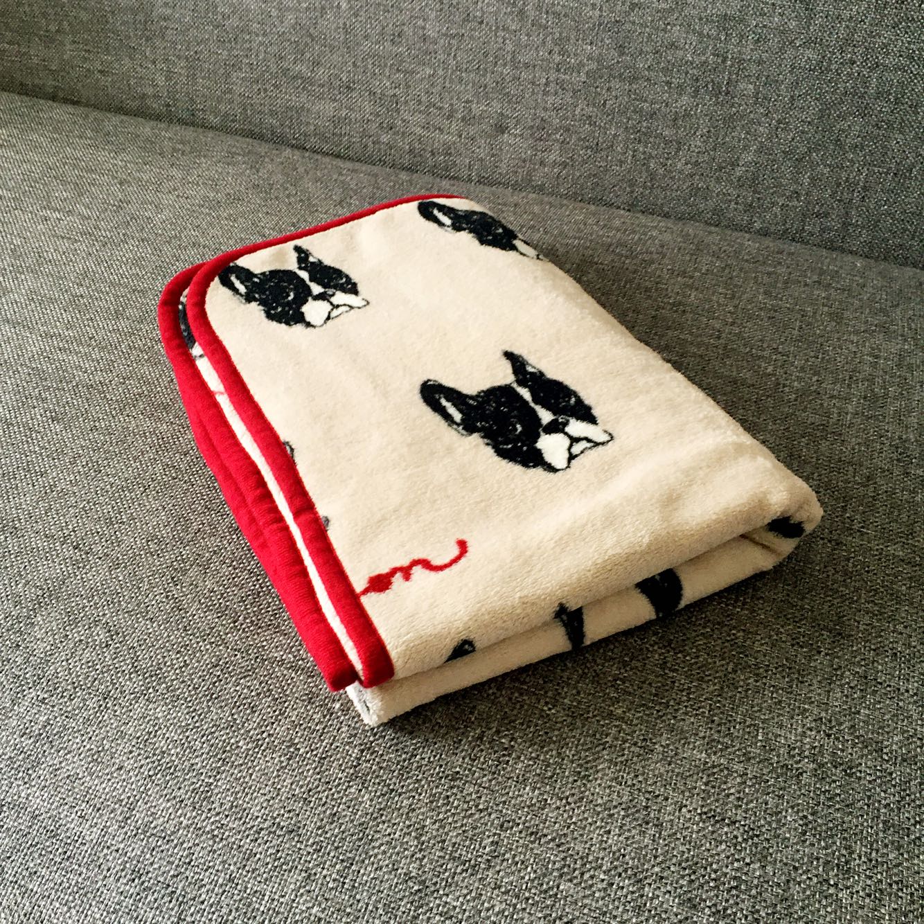 Folded beige pet blanket with black dog faces and red trim