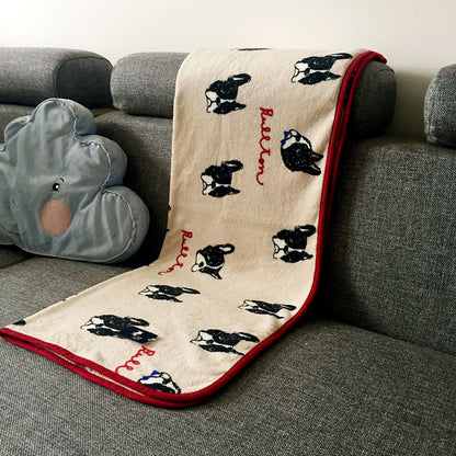 Beige pet blanket with scattered black dog faces and red border, draped on sofa