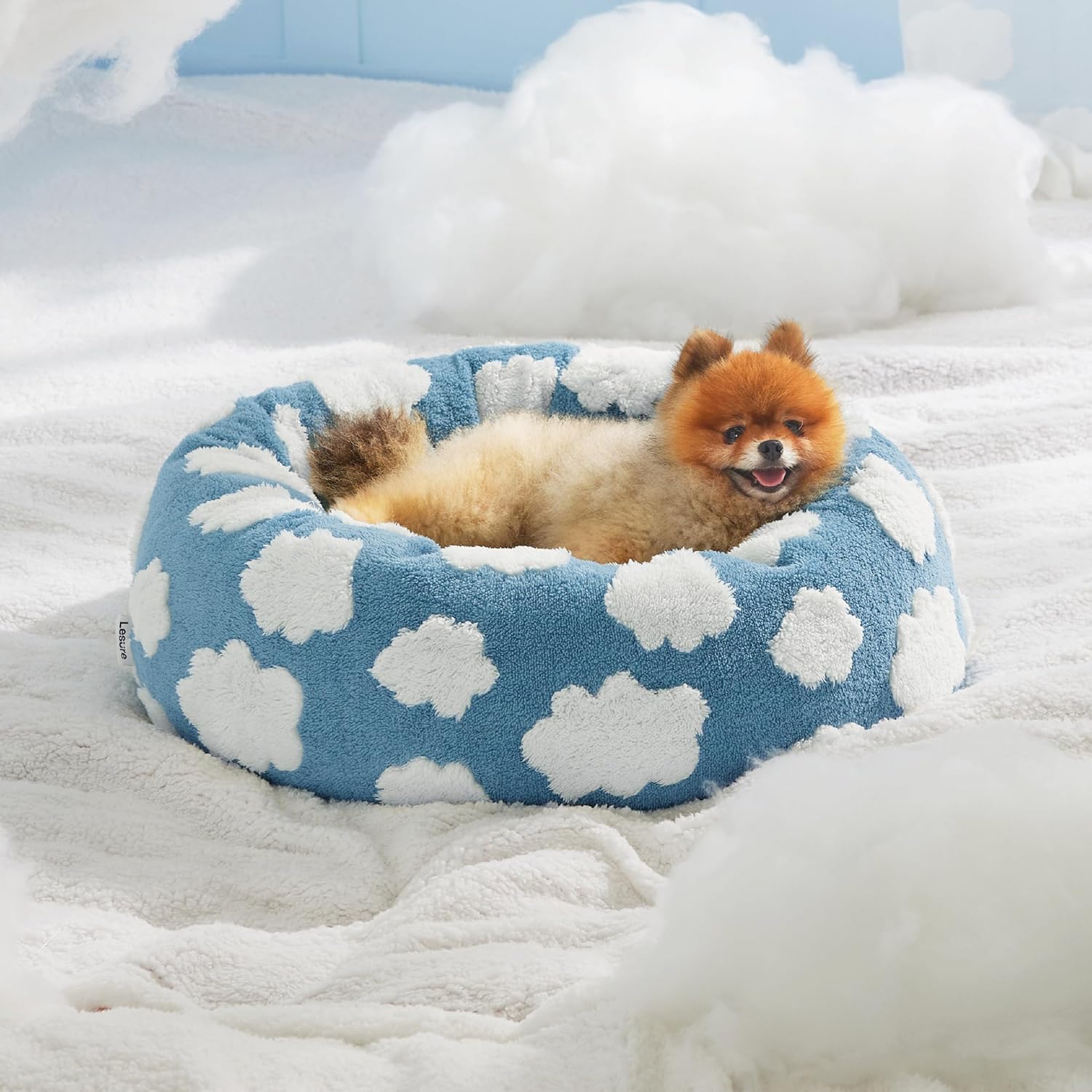 Blue plush round pet bed with white cloud pattern, small dog curled inside