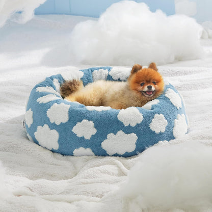 Blue plush round pet bed with white cloud pattern, small dog curled inside